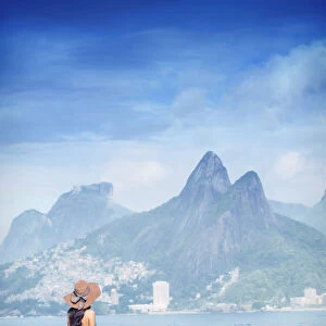 A 20-25 year old young Brazilian woman standing on the Arpoador rocks with Ipanema