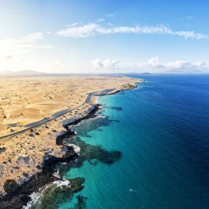 Aerial view of empty road beside the crystal turquoise ocean and sand dunes, Corralejo