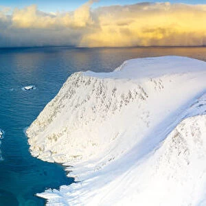 Aerial view of sunrise on snow capped mountains and blue arctic sea, Sorvaer