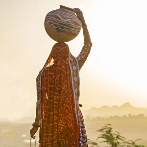 Ahir Woman in traditional colorful cloth carrying water in a clay jug on her head