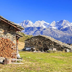 Alpine huts framed by snowy peaks of Bernina Group, Arcoglio Alp, Val Torreggio, Malenco Valley
