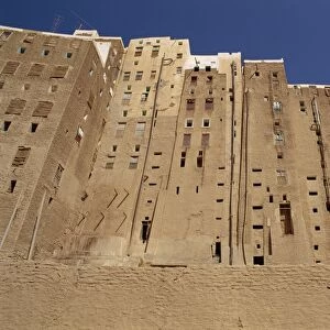 Backs of tall mud brick houses showing holes in the wall for toilets