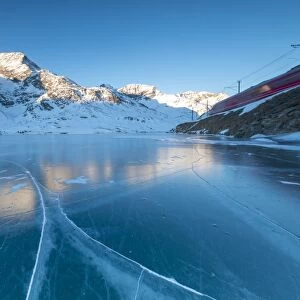 The Bernina Express train runs beside the frozen Lago Bianco, Bernina Pass, canton of Graubunden