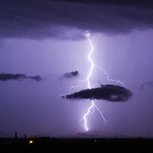 A bright lightning bolt passing through a cloud and striking in the Gila Bend Mountains