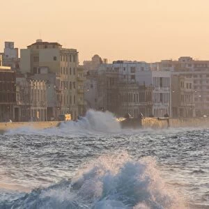 Buildings along The Malecon bathed in soft evening sunlight with large waves crashing against the sea wall, The Malecon, Havana, Cuba, West Indies, Caribbean, Central America