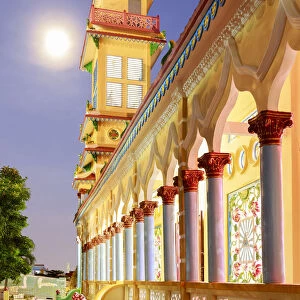 The Cao Dai temple in Vung Tau lit up at dusk with the full moon to the left of the tower