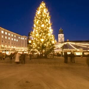 Christmas tree and stalls of historical Salzburg Christkindlmarkt (Christmas market) with Glockenspiel building, Residenzplatz at twilight, Salzburg