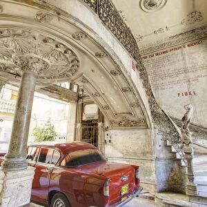 Classic red American car parked beneath ornate marble staircase inside dilapidated apartment building, Havana, Cuba, West Indies