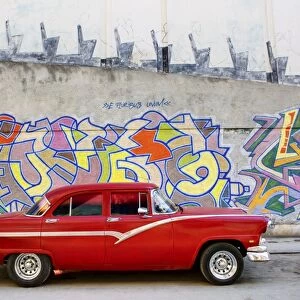 Classic red American car parked in front of grafitti covered wall, Havana