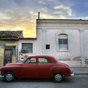 Classic red American car parked outside houses at sunset, Cienfuegos, Cuba
