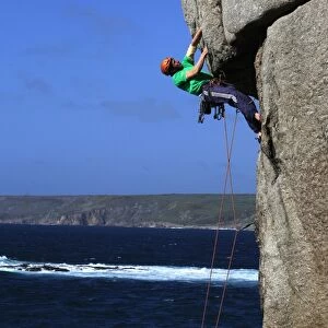 A climber tackles a difficult overhang on the cliffs near Sennen Cove, a popular rock climbing area at Lands End, Cornwall, England, United