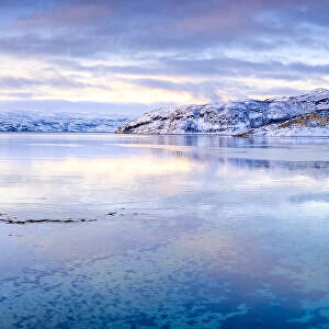 Clouds at sunset on snow capped mountains reflected in the clear water of Laksefjorden