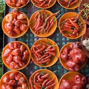Colourful red chillies and capsicums on orange plates on a market stall in Kuching