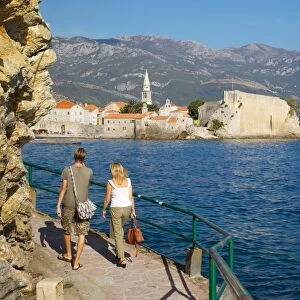 Couple walking along coast towards Old Town, Budva, Montenegro, Europe