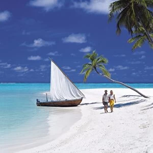 Couple walking on tropical beach and traditional dhoni, Maldives, Indian Ocean, Asia