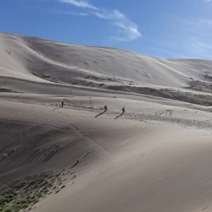 Distant people descending a huge sand dune, iridescent on a summer evening, Khongoryn Els