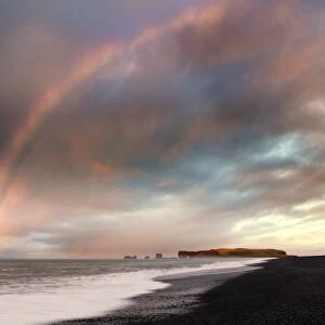 Distant view of Dyrholaey at sunrise with rainbow, from Halsanefs Hellir Beach near Vik