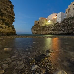 Dusk lights on the clear sea framed by the old town perched on the rocks, Polignano a Mare