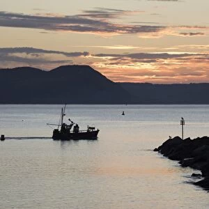 Fishing boat sailing past The Cobb at sunrise with Golden Cap and Jurassic Coast
