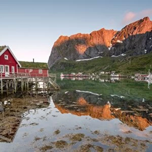 Fishing village and peaks reflected in water under midnight sun, Reine, Nordland county