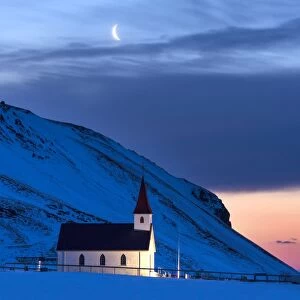 Floodlit church at dawn against snow covered mountains, winter, near Vik, South Iceland