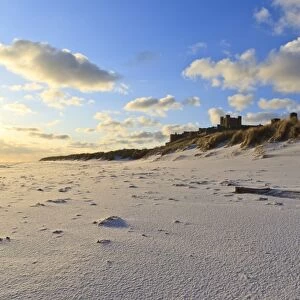 Fresh Spring snow at dawn highlight ripples and marks in the sand beneath Bamburgh Castle, Bamburgh, Northumberland, England