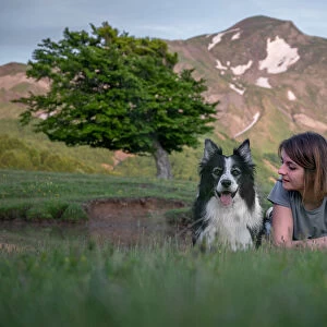 A girl and her border collie dog lying in the grass with a tree and mountain in the background, Emilia Romagna, Italy, Europe