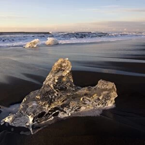 Glassy pieces of ice on volcanic black sand beach at sunrise, near Jokulsarlon Lagoon