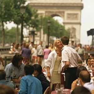 Greeting friends at an outdoor cafe on the Champs Elysees with the Arc de Triomphe behind