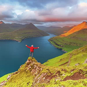 Happy hiker stands on top of the cliff overlooking the fjord of Funningur, Eysturoy island, Faroe islands, Denmark, Europe
