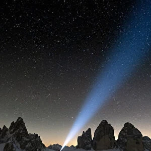 Hiker with head torch admiring stars on Monte Paterno and Tre Cime di Lavaredo