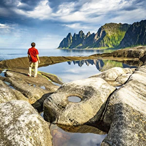 Hiker man contemplating the sharp rocks of mountain peaks standing beside rock pools
