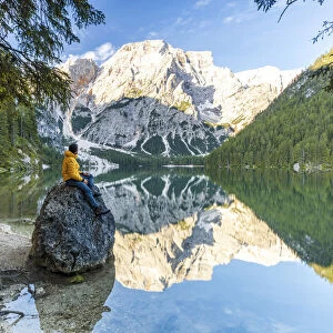 Hiker man enjoying sunrise sitting on rocks on shore of Lake Braies (Pragser Wildsee