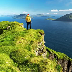 Hiker stands on top of a cliff admiring the rugged view, Nordradalur, Streymoy island, Faroe islands, Denmark, Europe