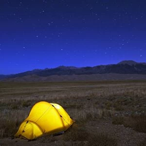 Hiker and tent illuminated under the night sky, Great Sand Dunes National Park