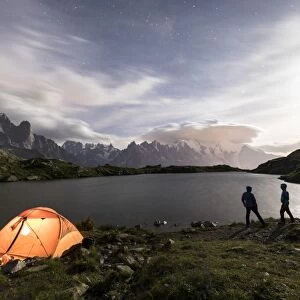 Hikers and tent on the shore of Lacs De Cheserys at night with Mont Blanc massif in the background