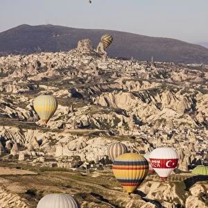Hot air balloons flying among rock formations at sunrise in the Red Valley, Goreme National Park