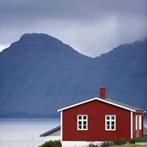 Houses at Hellur, small village near Oyndarfjordur, cliffs of Kalsoy Island in background