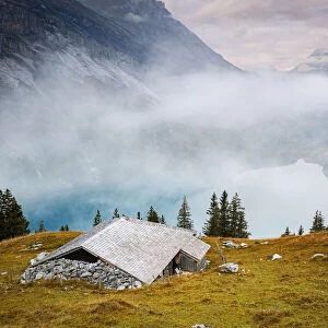 Hut on mountain ridge above lake Oeschinensee covered by mist, Bernese Oberland