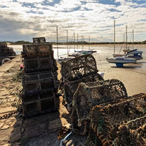 Lobster pots on harbour wall and yachts on beach at low tide on a summer evening
