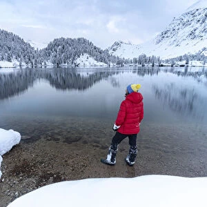 Man standing on shores of Lake Cavloc admiring the snowy woods, Bregaglia Valley