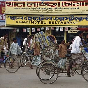 Men riding cycle rickshaws on the street passing the outside of a hotel