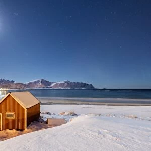 Moonlight on a typical fishermen cabin surrounded by snow, Ramberg, Flakstad, Nordland County