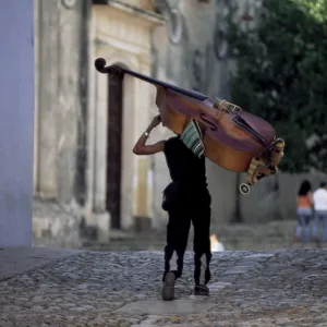 Musician carrying double bass along cobbled street to Plaza Mayor, Trinidad