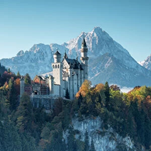 Neuschwanstein Castle surrounded by colorful woods and snowy peaks, Fussen, Bavaria