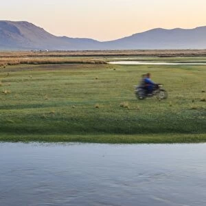 Nomads on motorcycle pass in a blur, river and distant gers, dawn, Nomad camp, Gurvanbulag