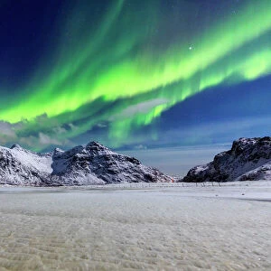 Northern Lights (aurora borealis) illuminate the sky and the snowy peaks, Flakstad