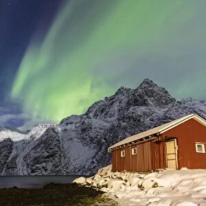 Northern Lights (aurora borealis) illuminate snowy peaks and the wooden cabin