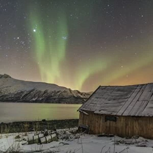 The Northern Lights illuminates the wooden cabin, Svensby, Lyngen Alps, Troms, Lapland