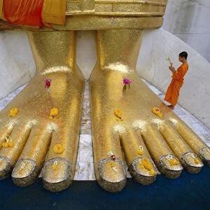 Novice monk praying at the feet of Giant Buddha statue